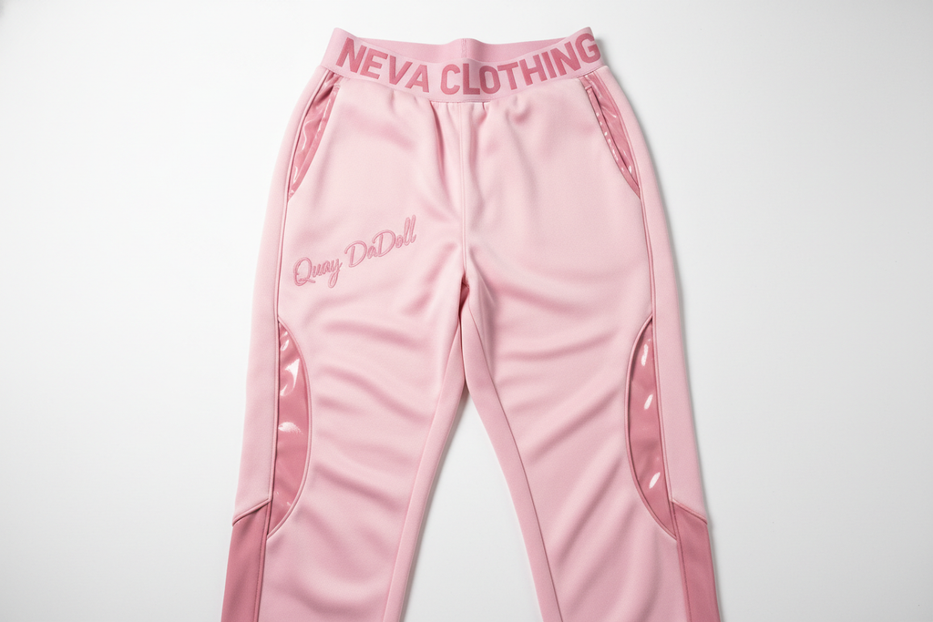 Women’s pink Quay DaDoll joggers in a stylish streetwear design. Semi-baggy fit with soft curves, glossy accents, and a high waistband that reads ‘NEVA Clothing’ in bold lettering, with ‘Quay DaDoll’ scripted along the hip. Two-tone pink palette, feminine urban fashion vibe, premium fabric texture, studio lighting.”